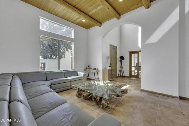 tiled living room with baseboards, arched walkways, a towering ceiling, wooden ceiling, and beam ceiling