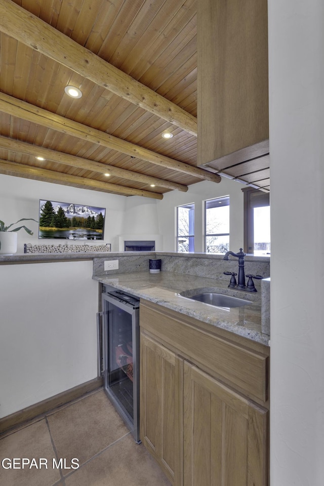 kitchen featuring wood ceiling, wine cooler, light stone counters, a sink, and beam ceiling