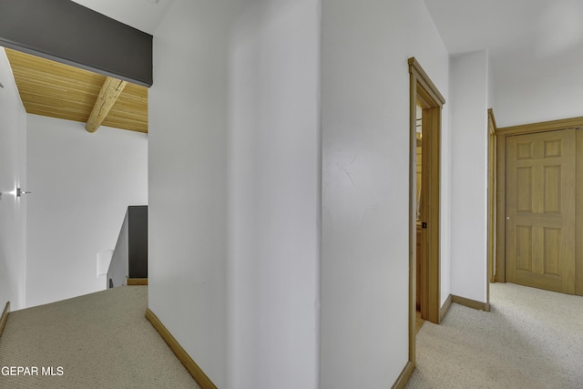 corridor featuring carpet, baseboards, beamed ceiling, and an upstairs landing