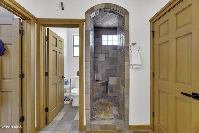 bathroom with toilet, baseboards, and a tile shower