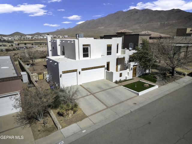 view of front of home featuring driveway, an attached garage, a mountain view, and stucco siding