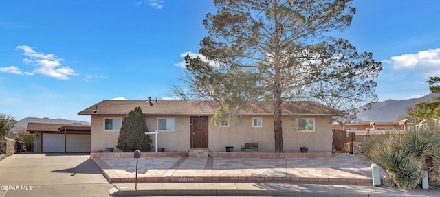 ranch-style house with fence, driveway, an attached garage, stucco siding, and a mountain view