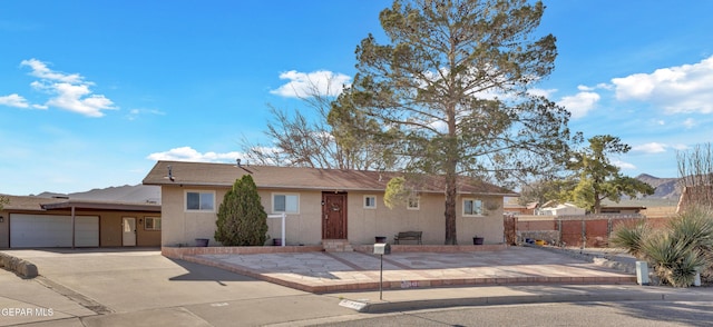 single story home with stucco siding, an attached garage, driveway, and fence