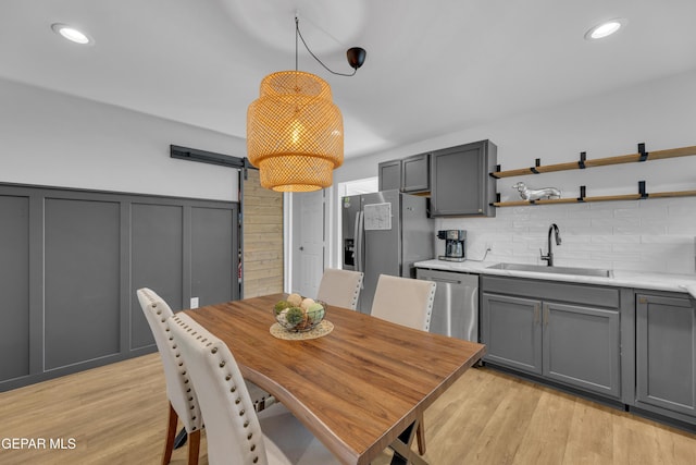 dining area with a wainscoted wall, light wood-style flooring, recessed lighting, a barn door, and a decorative wall