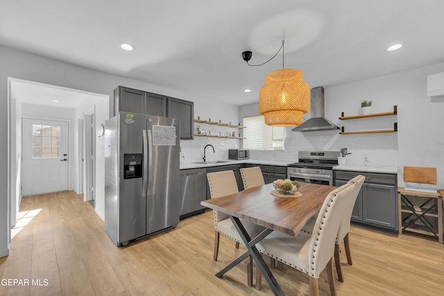 kitchen with open shelves, a sink, stainless steel appliances, wall chimney exhaust hood, and light wood-type flooring