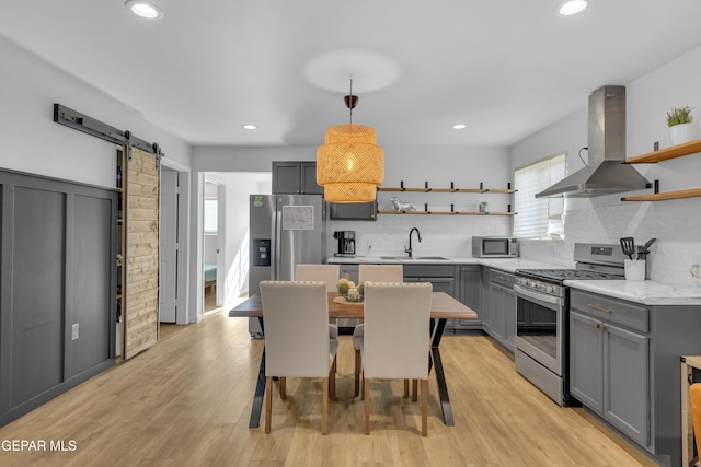 kitchen with gray cabinetry, open shelves, a barn door, appliances with stainless steel finishes, and extractor fan