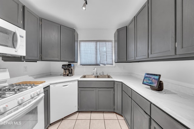 kitchen featuring gray cabinetry, light countertops, light tile patterned floors, white appliances, and a sink