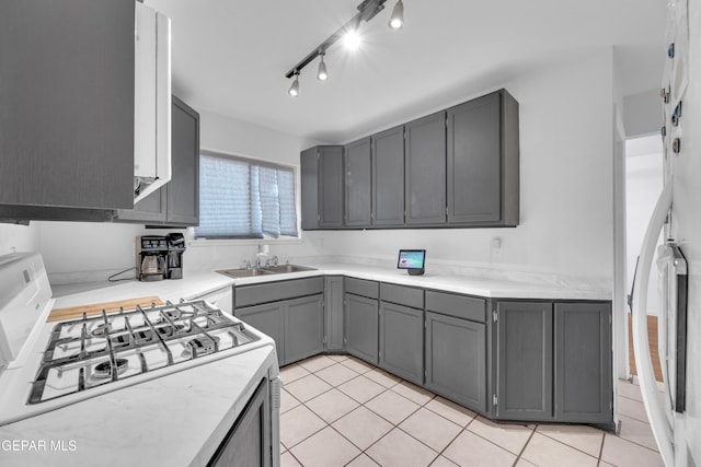 kitchen with light countertops, gas range oven, light tile patterned floors, fridge, and a sink