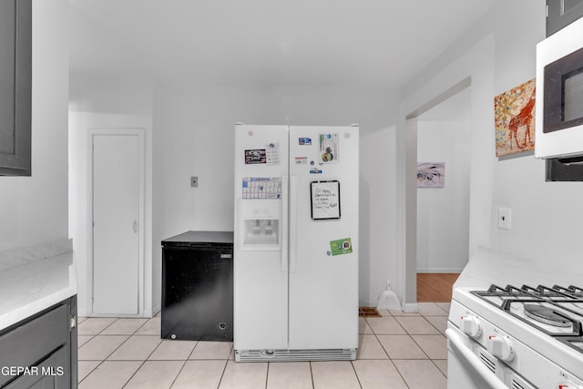 kitchen featuring light tile patterned floors, light stone counters, white appliances, and baseboards