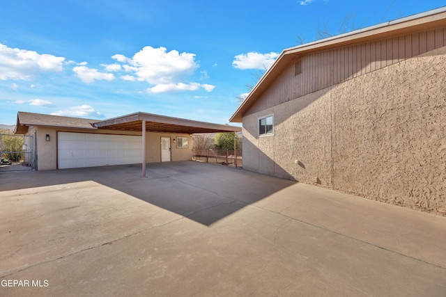 view of side of home with stucco siding, a carport, concrete driveway, and fence