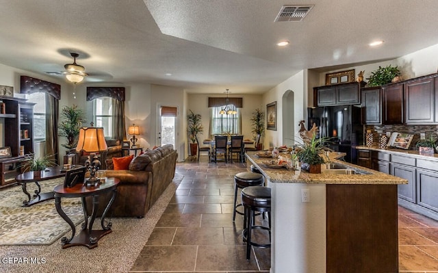 kitchen with light stone counters, visible vents, decorative backsplash, freestanding refrigerator, and a kitchen bar