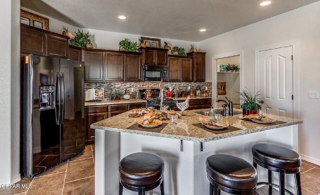 kitchen featuring black appliances, a breakfast bar, a sink, and dark brown cabinets