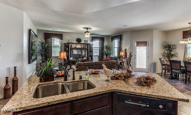 kitchen with dark brown cabinetry, a sink, open floor plan, light stone countertops, and dishwasher