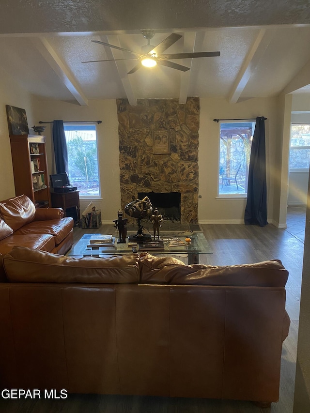 living area with baseboards, a textured ceiling, a stone fireplace, and wood finished floors