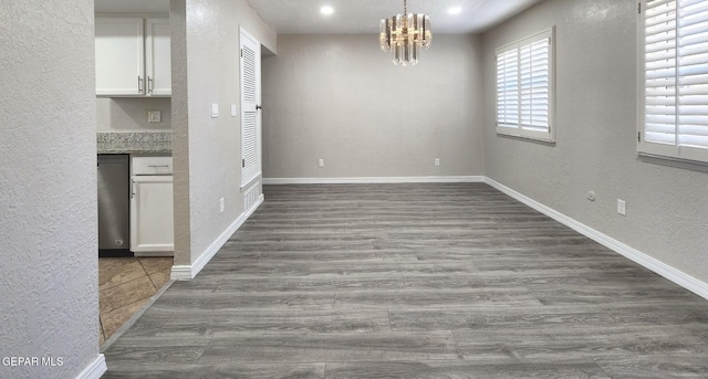 unfurnished dining area featuring baseboards, an inviting chandelier, dark wood finished floors, and a textured wall