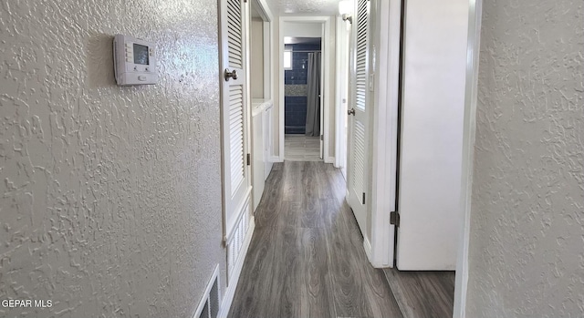 hallway featuring visible vents, wood finished floors, and a textured wall