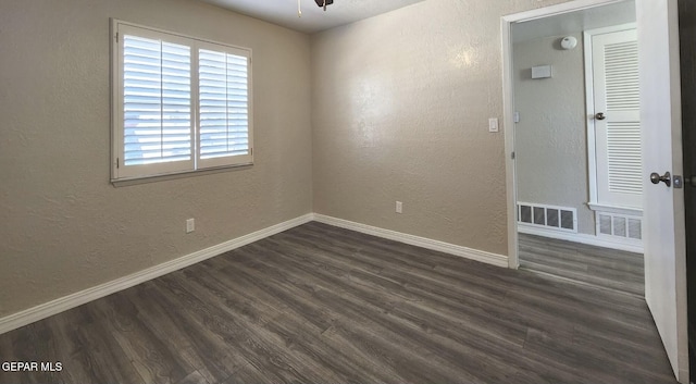 spare room with dark wood-type flooring, a textured wall, visible vents, and baseboards