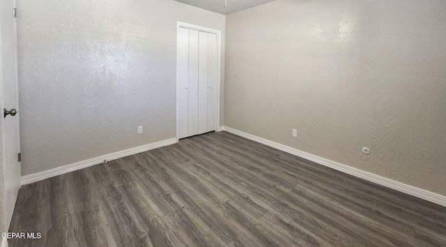 unfurnished bedroom with a closet, dark wood-type flooring, baseboards, and a textured wall