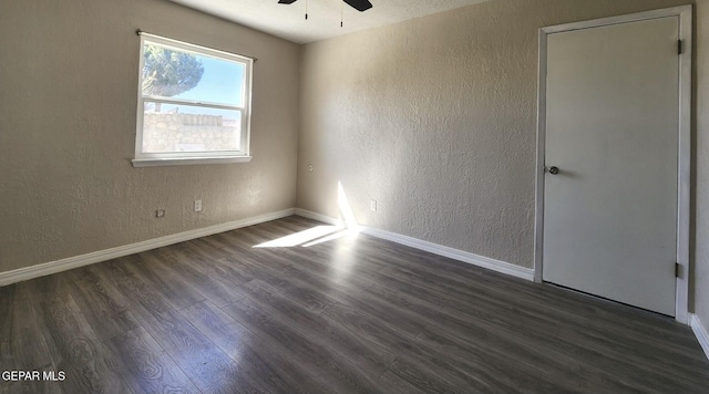 empty room with dark wood finished floors, a textured wall, baseboards, and a ceiling fan