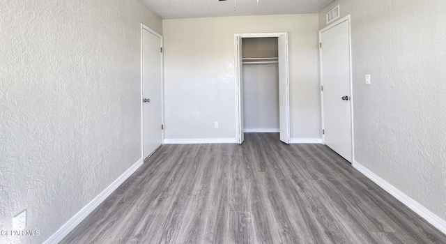 unfurnished bedroom featuring visible vents, baseboards, wood finished floors, and a textured wall