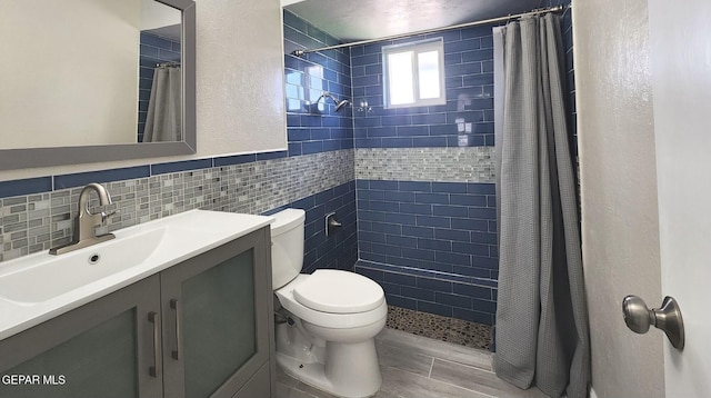 full bath featuring a tile shower, toilet, vanity, and a textured wall