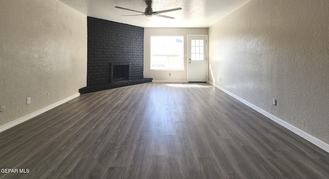 unfurnished living room with dark wood-style flooring, ceiling fan, a textured ceiling, a brick fireplace, and a textured wall