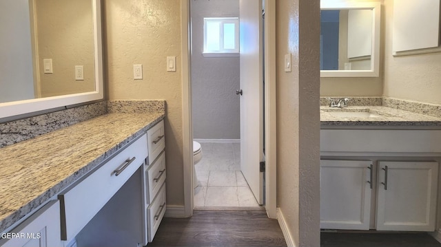 bathroom featuring baseboards, toilet, vanity, and a textured wall