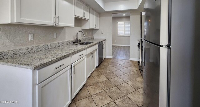 kitchen with baseboards, light stone counters, stainless steel appliances, white cabinetry, and a sink