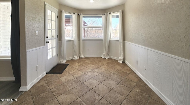 doorway featuring wainscoting and a textured wall