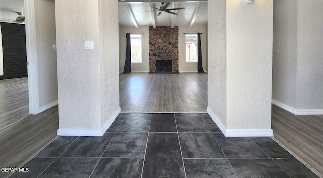 unfurnished living room with a stone fireplace, beamed ceiling, baseboards, and ceiling fan