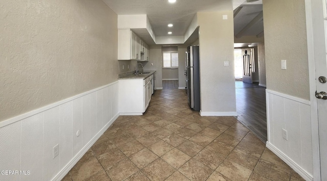 kitchen with white cabinets, freestanding refrigerator, a textured wall, and a sink