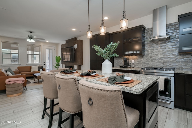 kitchen with wall chimney exhaust hood, backsplash, a kitchen island, stainless steel gas range oven, and a kitchen bar