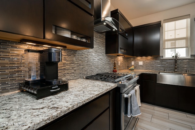 kitchen with decorative backsplash, light stone countertops, stainless steel gas range, range hood, and a sink