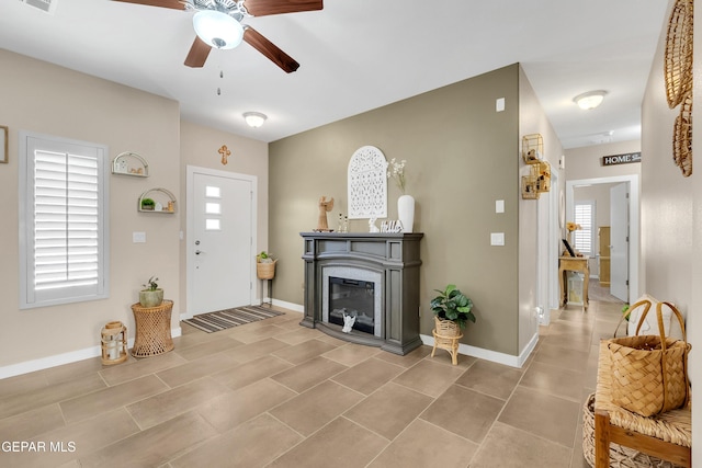 entrance foyer with ceiling fan, a glass covered fireplace, visible vents, and baseboards