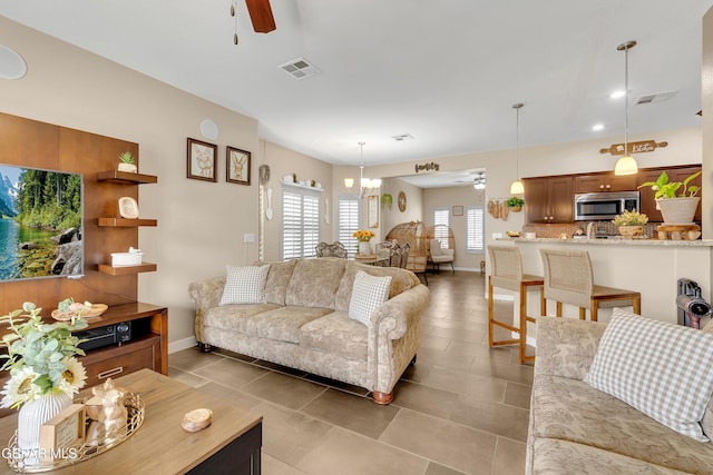 living area with light tile patterned floors, baseboards, visible vents, and ceiling fan with notable chandelier