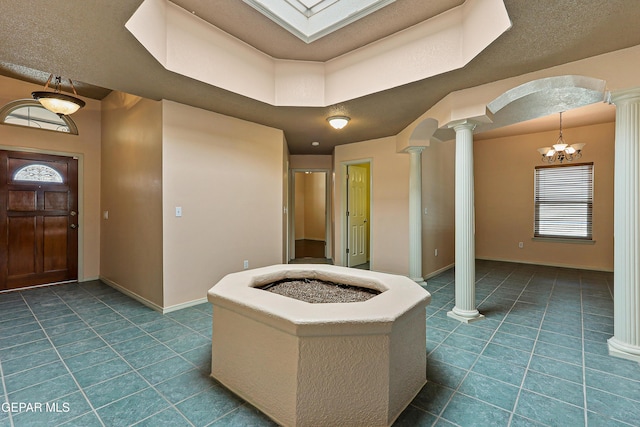 foyer entrance with dark tile patterned flooring, baseboards, arched walkways, and ornate columns