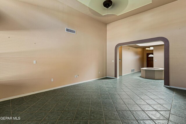 empty room featuring visible vents, arched walkways, baseboards, and ceiling fan