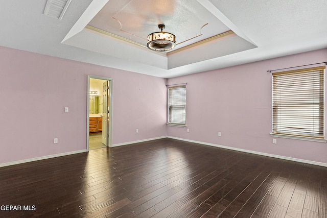 spare room with baseboards, a tray ceiling, and wood finished floors