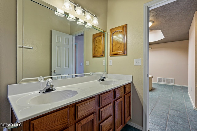 bathroom featuring double vanity, visible vents, a textured ceiling, and a sink