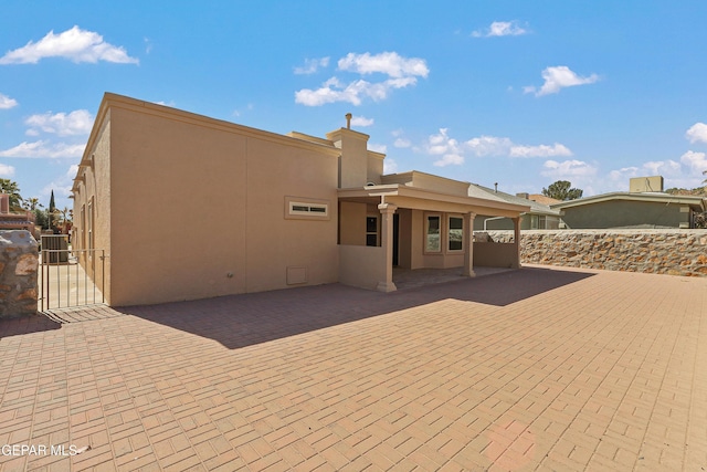 rear view of property featuring stucco siding, a patio, fence, and a gate