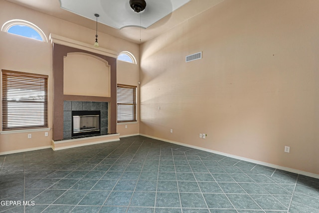 unfurnished living room featuring a tiled fireplace, visible vents, baseboards, and dark tile patterned floors