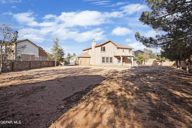 rear view of house featuring stucco siding, fence, and a chimney