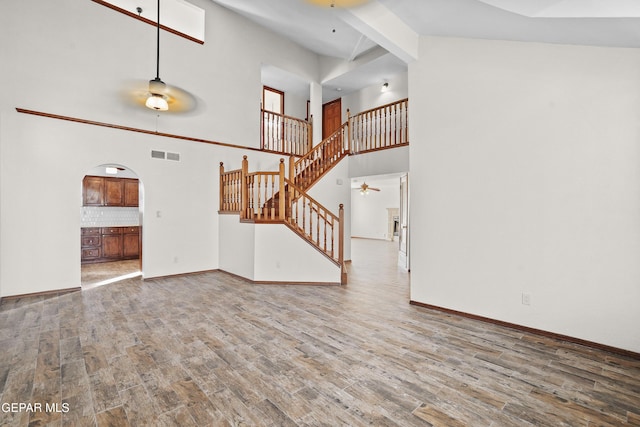 unfurnished living room with visible vents, a ceiling fan, wood finished floors, stairway, and arched walkways