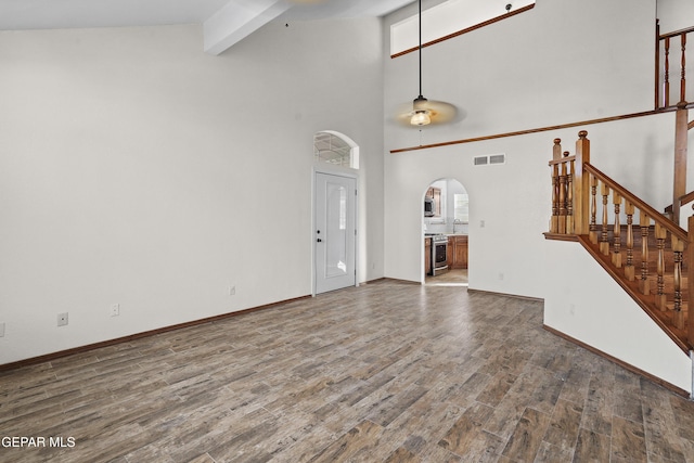 unfurnished living room featuring wood finished floors, visible vents, beam ceiling, arched walkways, and stairs