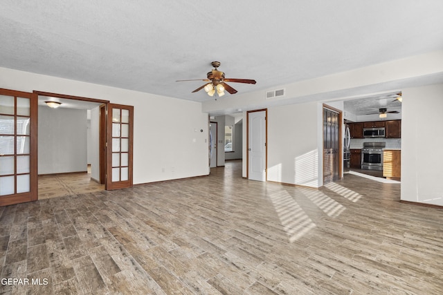 unfurnished living room with visible vents, french doors, ceiling fan, and wood finished floors