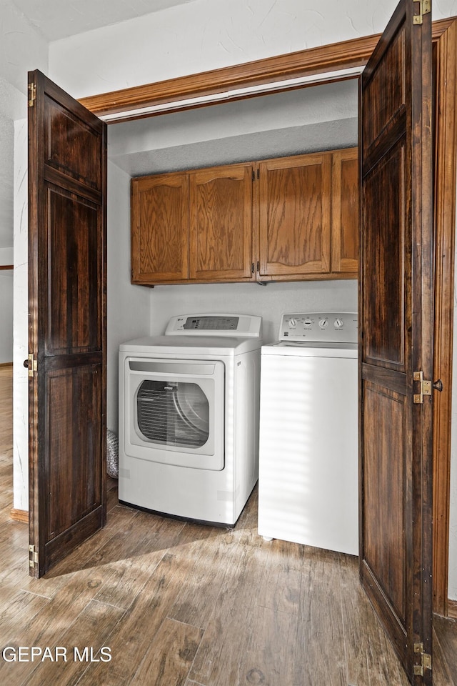 washroom featuring washer and clothes dryer, cabinet space, and wood finished floors