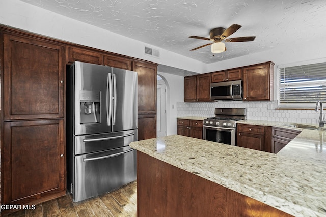 kitchen with wood finished floors, arched walkways, a sink, appliances with stainless steel finishes, and tasteful backsplash