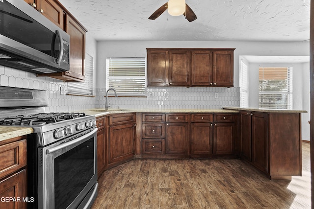 kitchen featuring dark wood-style floors, a peninsula, a sink, stainless steel appliances, and a textured ceiling