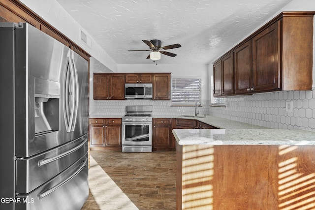 kitchen with a peninsula, a sink, ceiling fan, stainless steel appliances, and backsplash