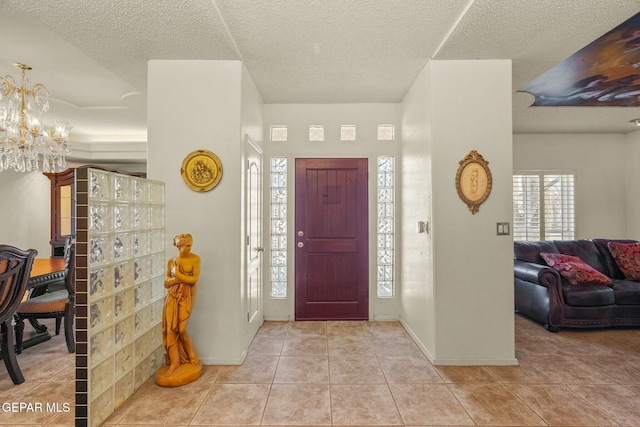 foyer entrance with a chandelier, tile patterned flooring, a textured ceiling, and baseboards